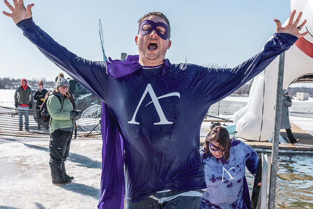 An excited man wearing a purple Affinity Plus T-shirt raises his arms in the air after taking the Polar Plunge