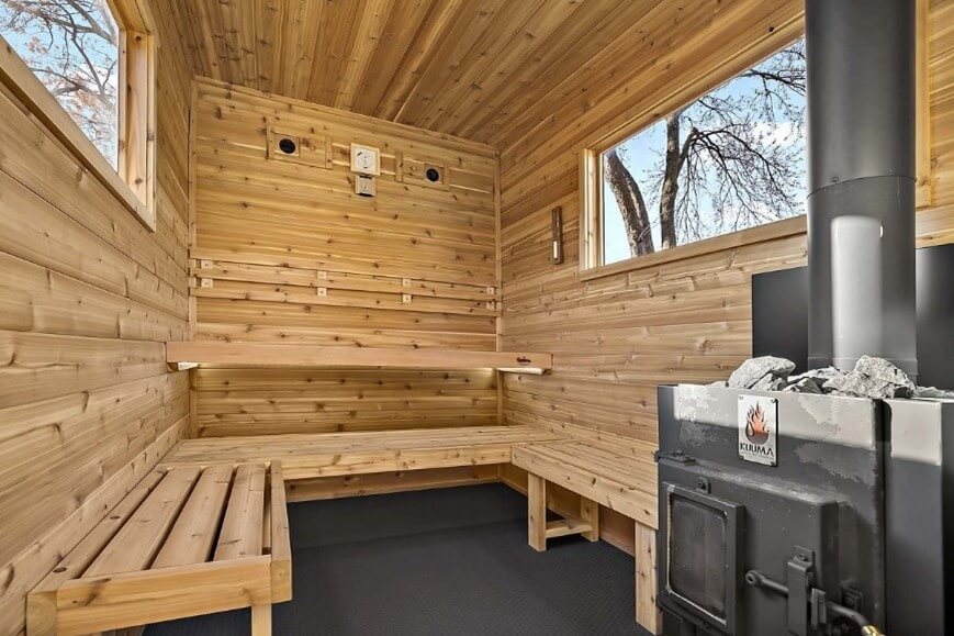 Photo of the inside of a portable sauna, including wooden benches, two windows and a small black stove